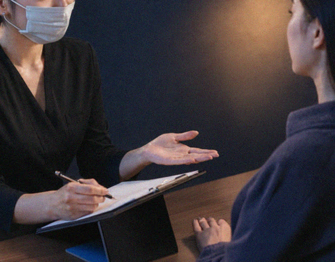 A Pharmesthetic practitioner taking notes on a clipboard while consulting a client across a table
